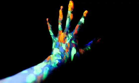 A hand covered in glow in the dark paint, creating a mesmerizing and luminous effect. A passionate scene where two lovers immerse in each other