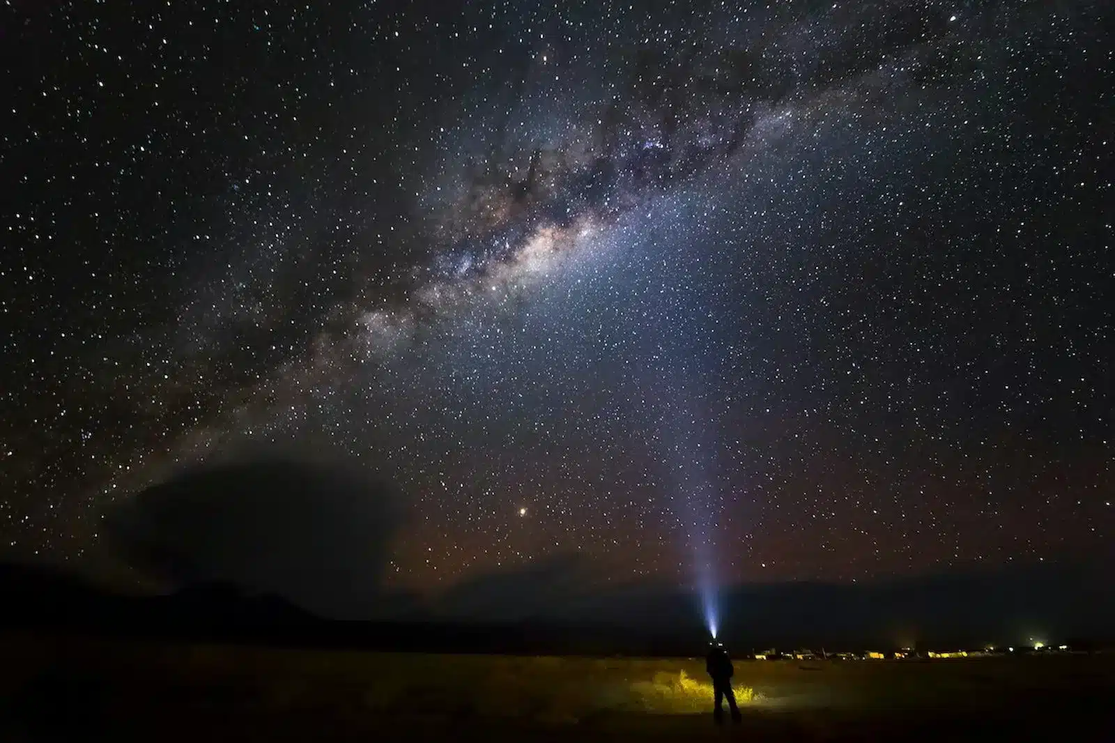 Image of a man stands before a starry sky, holding a flashlight. Trust your heart, embrace its wisdom, and persist, even in darkness