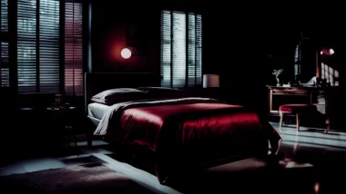 Image of a darkly light bedroom with a bed draped in red silk sheets with a red theme. The image captures the intense scene of the installment that takes place a bedroom