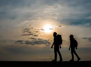 Adventurous couple with backpacks silhouetted against vibrant sunset - The Adventures of Griffin and Karen short story series